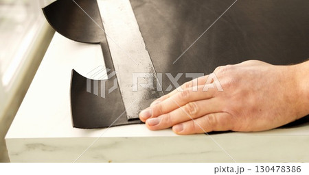 Craftsman aligning leather sheet with ruler during work in studio. 130478386