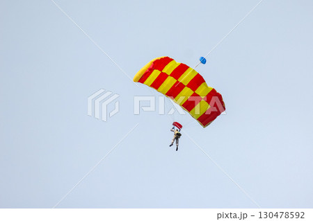 Skydiver descends with colorful parachute over open sky during bright daylight Skydiver descends with colorful parachute over open sky during bright daylight 130478592