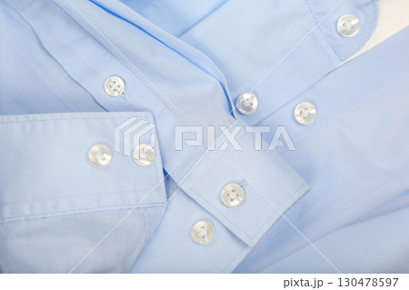 Close-up view of light blue shirt fabric with buttons showing intricate detail and texture Close-up view of light blue shirt fabric with buttons showing intricate detail and texture 130478597