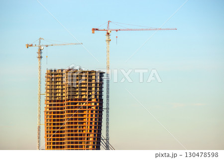 Construction of a high-rise building with cranes against a clear blue sky Construction of a high-rise building with cranes against a clear blue sky 130478598