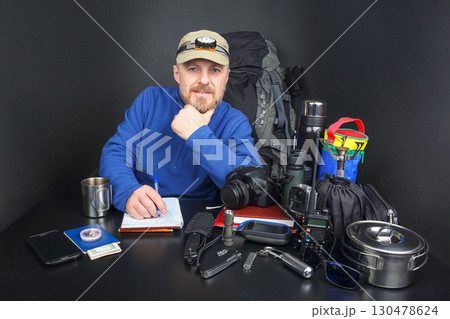 Outdoor enthusiast prepares for adventure with gear and supplies at a table indoors Outdoor enthusiast prepares for adventure with gear and supplies at a table indoors 130478624