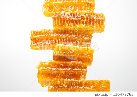 Honeycomb pieces stacked vertically showing golden honey glistening under bright light 130478763