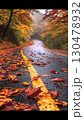 Winding road with wet asphalt covered in vibrant fallen leaves meandering through misty autumn forest, revealing seasonal color palette and moody woodland landscape 130478932