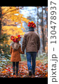 Father and young daughter walking hand in hand through golden forest, wearing maple leaf crowns, sharing warm autumn moment surrounded by vibrant fall colors 130478937