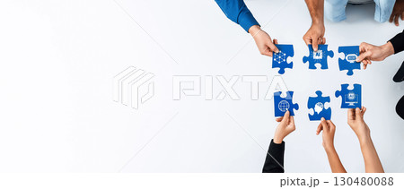 Collaborative teamwork concept featuring hands holding puzzle pieces with diverse icons representing global cooperation and problem-solving in a modern workspace. Amity 130480088