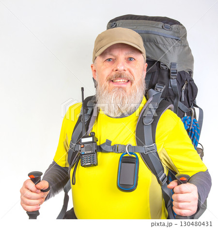 A smiling bearded hiker in a yellow shirt and cap holds trekking poles 130480431