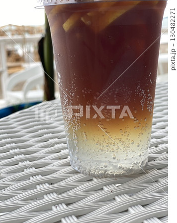 Iced tea in a clear plastic cup with lemon slices and bubbles, on woven table, seaside background 130482271