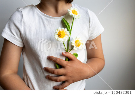 Young child holding handmade crochet flowers in white shirt 130482391