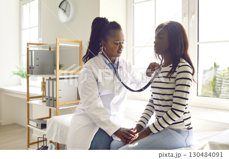 Female doctor with stethoscope examining woman's lungs and heartbeat in medical office. 130484091