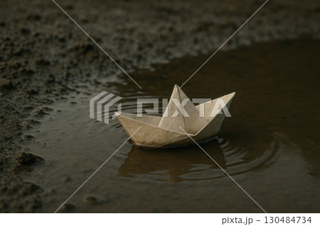 A paper ship floats in a small puddle on the ground. A paper ship floats in a small puddle on the ground. 130484734