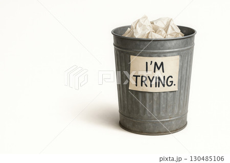 Metal trash can with paper and I'M TRYING written on a white background. Space for text. 130485106