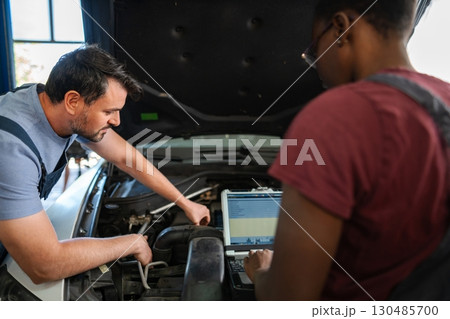 Two mechanics repairing a car engine using a computer diagnostic software Two mechanics repairing a car engine using a computer diagnostic software 130485700