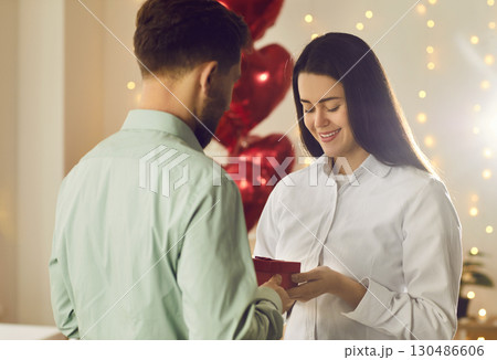 Man holding red present box in his hand and congratulating pretty woman on holiday. Man holding red present box in his hand and congratulating pretty woman on holiday. 130486606