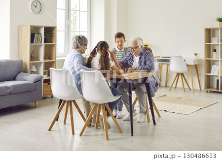 Grandparents and children are playing chess at the table in the living room at home 130486613