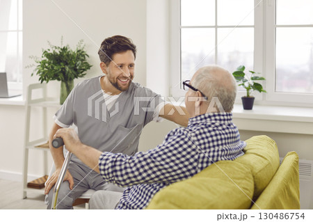 Optimistic male caregiver comforting senior patient, touching his shoulder 130486754