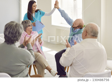 Seniors doing high five in a group therapy session with a young nurse in nursing home. Seniors doing high five in a group therapy session with a young nurse in nursing home. 130486756
