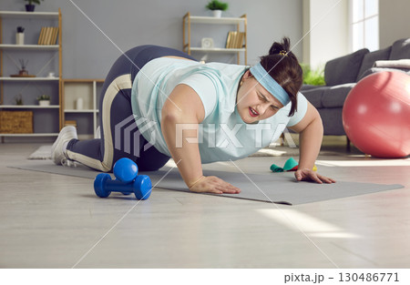 Tired overweight woman trying to do difficult push ups on an exercise mat at home 130486771