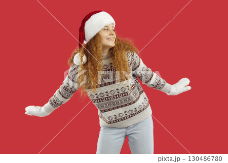 Dancing playful funny redhead girl in Christmas Santa hat and sweater on red background. Dancing playful funny redhead girl in Christmas Santa hat and sweater on red background. 130486780