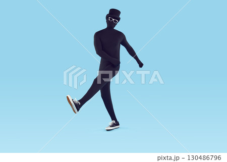 Faceless man wearing black bodysuit costume with hat and glasses walking on blue background. 130486796