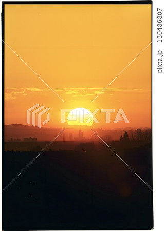 A bright sunset dominates the horizon, casting an intense orange glow over distant mountains and a silhouetted cityscape. 130486807