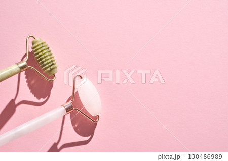 Jade and rose quartz facial rollers on pink background for skincare routine 130486989