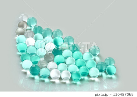 Arrangement of translucent aqua and white marbles on reflective surface 130487069
