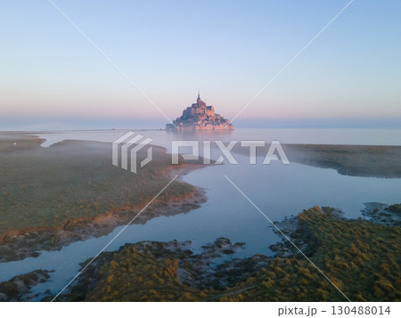 The iconic Mont Saint-Michel emerges through thick fog on a gloomy day, with its medieval village and abbey shrouded in mist on the Normandy coast The iconic Mont Saint-Michel emerges through thick fog on a gloomy day, with its medieval village and abbey shrouded in mist on the Normandy coast 130488014
