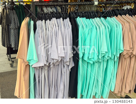 Close view of colorful t-shirts hanging in street retail market. Shopping, fashion, and lifestyle consumer concept in outdoor commerce. 130488143