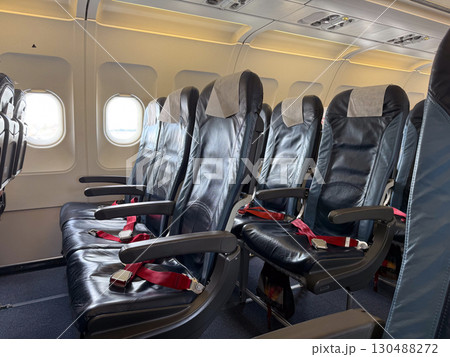 Empty black leather airplane seats next to a window with seatbelts placed on the cushions. Travel, aviation, and the arrangement of seating for passengers on modern flights. 130488272