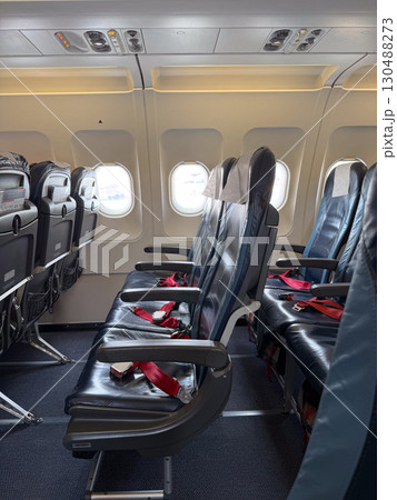 Empty black leather airplane seats next to a window with seatbelts placed on the cushions. Travel, aviation, and the arrangement of seating for passengers on modern flights. 130488273