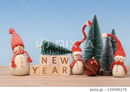 Christmas background with knitted snowmen in red hats and Christmas trees with red ball and wooden cubes with the word New Year on them. Christmas and New Year design holiday card 130490278