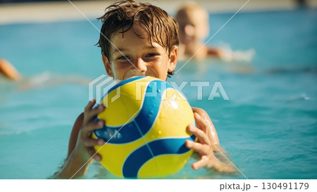 Cheerful young boy playing with vibrant inflatable ball, splashing in swimming pool, enjoying sunny summer day and cool water 130491179