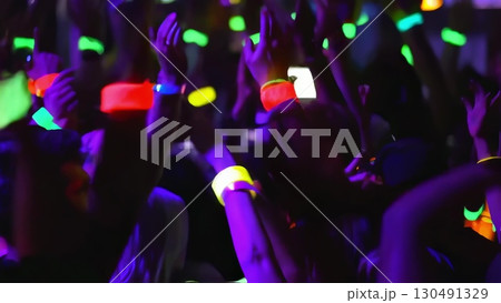 Concert crowd waving colorful glow sticks, generating electric atmosphere with synchronized movements, radiating music festival excitement and shared musical passion 130491329