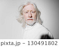 Portrait of an elderly man with long white hair and beard, wearing a white outfit against a soft gray background, conveying a sense of wisdom, serenity, and timeless elegance 130491802