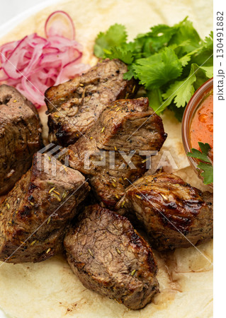 Traditional Georgian grilled meat (mtsvadi) with onion, herbs, and sauce on lavash 130491882