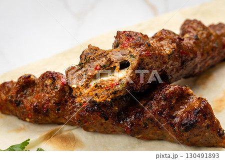 Close-up of grilled kebab with melted cheese inside on flatbread, juicy and spicy Close-up of grilled kebab with melted cheese inside on flatbread, juicy and spicy 130491893