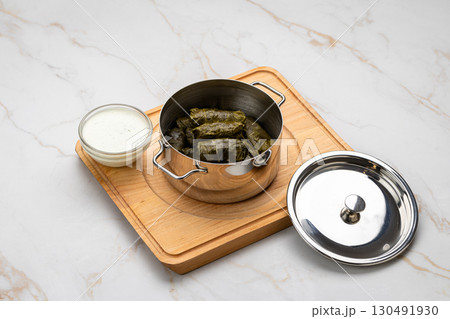 Stuffed grape leaves called dolma in steel pot with yogurt sauce on wooden board 130491930
