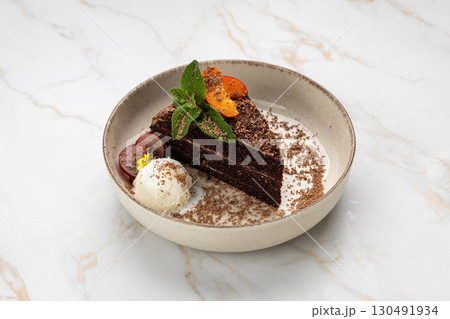 Chocolate cake slice with ice cream, grapes, mint and fruit on elegant white ceramic plate 130491934