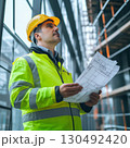 Professional engineer wearing high visibility jacket and hardhat examining blueprints on a construction site, ensuring project compliance and safety regulations 130492420