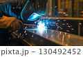 Skilled welder in protective gear joins metal parts with a torch, creating bright sparks in an industrial workshop. The image showcases craftsmanship, labor, and safety in metal fabrication 130492452