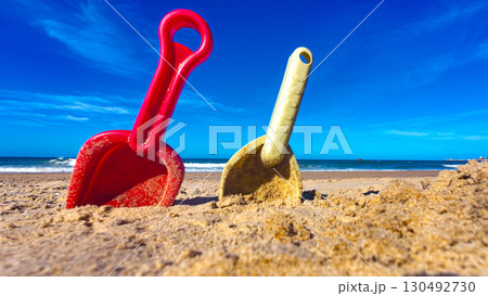 Colorful plastic shovels stuck in the sand on a sunny beach with blue sky Colorful plastic shovels stuck in the sand on a sunny beach with blue sky 130492730