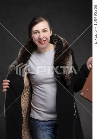 Happy fifty year old woman in a coat with a fur collar on a gray background. Portrait of a middle-aged woman. 130495268