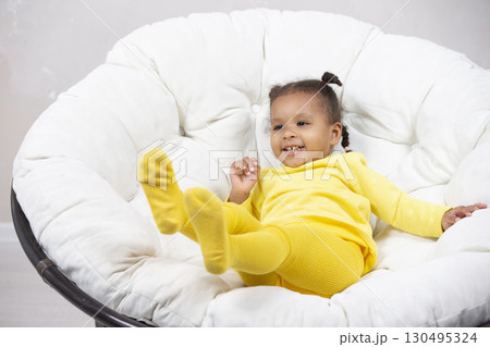 Little African American girl indulges and plays in an easy chair. 130495324
