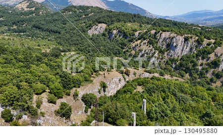 Vibrant green valleys and rugged cliffs embrace the landscape of a tranquil mountain region during bright daylight hours 130495880