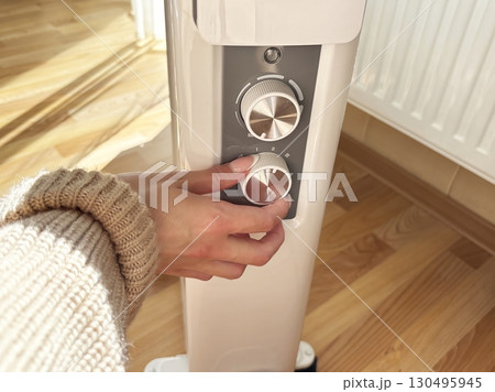 Woman hand adjusts heater control panel to change heating power. Cold weather, beginning of heating season, regulating and adjusting room temperature, home heating comfort Woman hand adjusts heater control panel to change heating power. Cold weather, beginning of heating season, regulating and adjusting room temperature, home heating comfort 130495945
