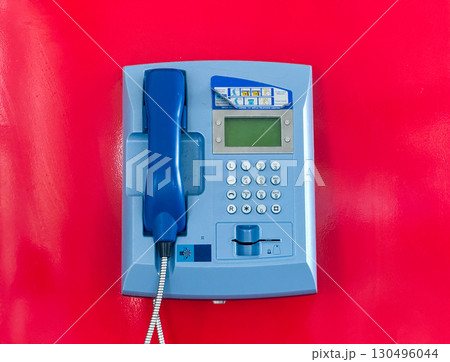 Blue public telephone on a red wall in a modern building. Communication, technology, and public service equipment for contact and emergency use in an airport interior. Blue public telephone on a red wall in a modern building. Communication, technology, and public service equipment for contact and emergency use in an airport interior. 130496044