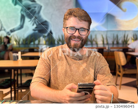 Man sitting in a lounge chair while looking at his phone. Technology, communication, and leisure illustrated through travel waiting moments and everyday digital habits. Man sitting in a lounge chair while looking at his phone. Technology, communication, and leisure illustrated through travel waiting moments and everyday digital habits. 130496045