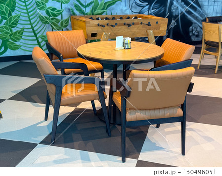 Round wooden table with leather chairs in a cafe interior near foosball game. Socialization, dining, and leisure illustrated as part of travel lifestyle and hospitality culture. 130496051