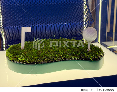 Golf ball placed on green artificial grass with miniature flag. Representation of leisure, competition, and recreation culture highlighting hobby and sports lifestyle. 130496059