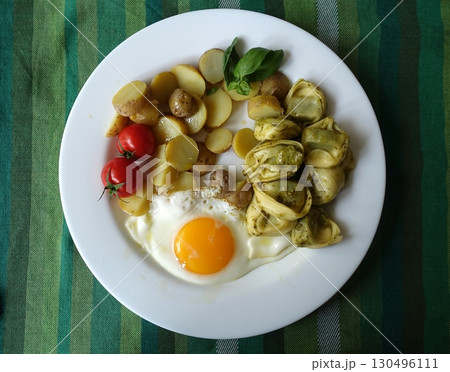 A vegetarian dish with pesto tortellini, a fried egg, new potato salad, cherry tomatoes, and a basil sprig. 130496111